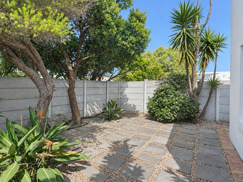 A well-maintained rear courtyard featuring a paved patio area, established trees, and a secure precast concrete boundary wall.