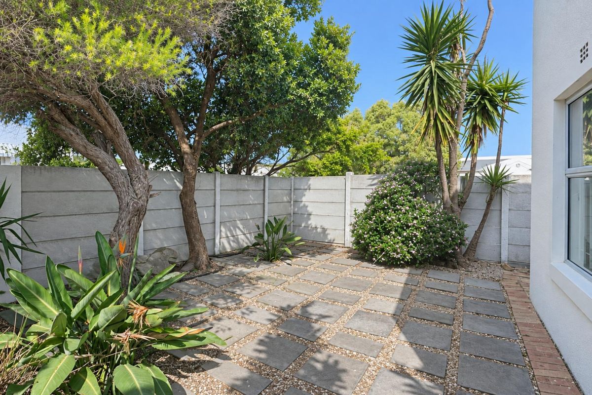 A well-maintained rear courtyard featuring a paved patio area, established trees, and a secure precast concrete boundary wall.