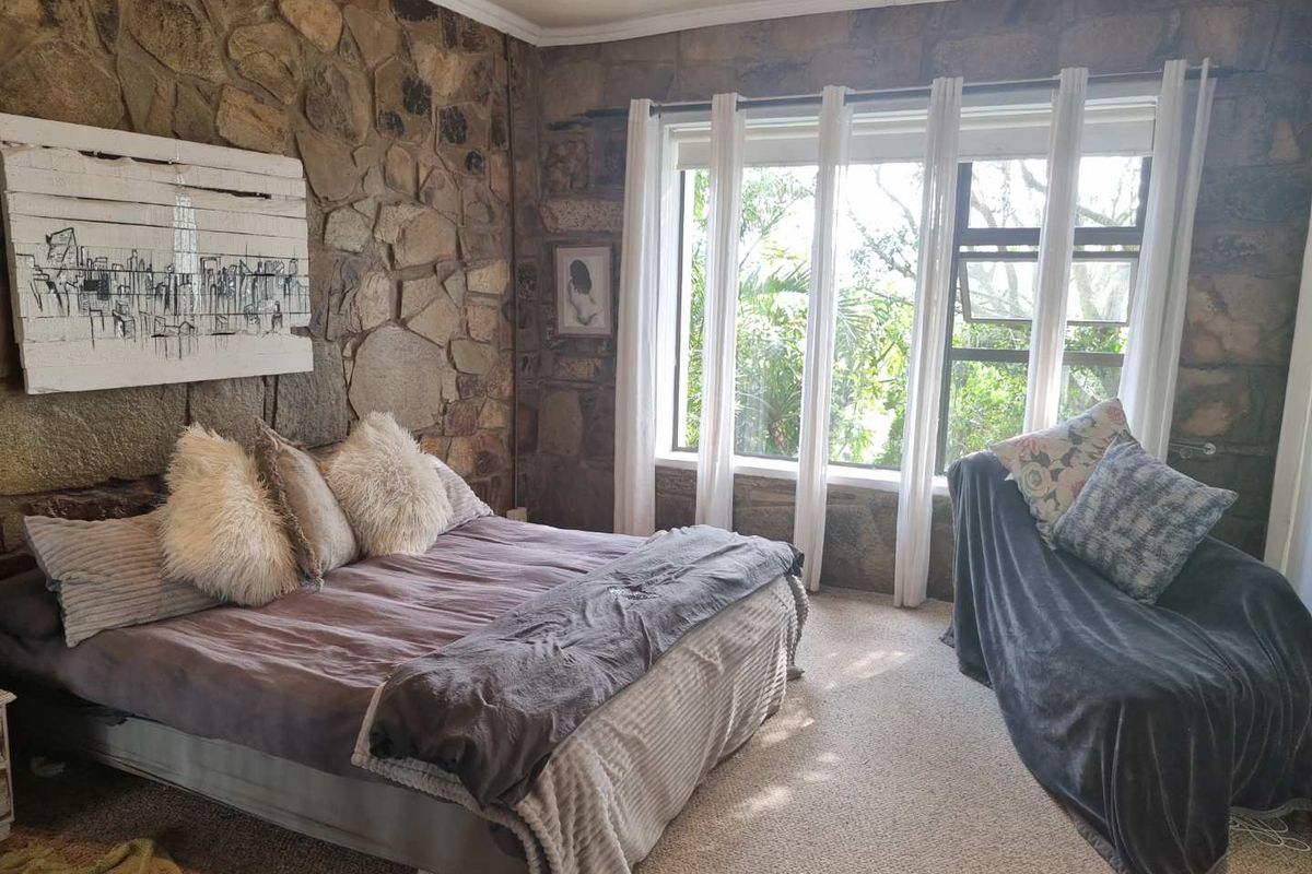 A bedroom featuring a prominent natural stone feature wall, large windows with garden views, and recessed ceiling lighting.