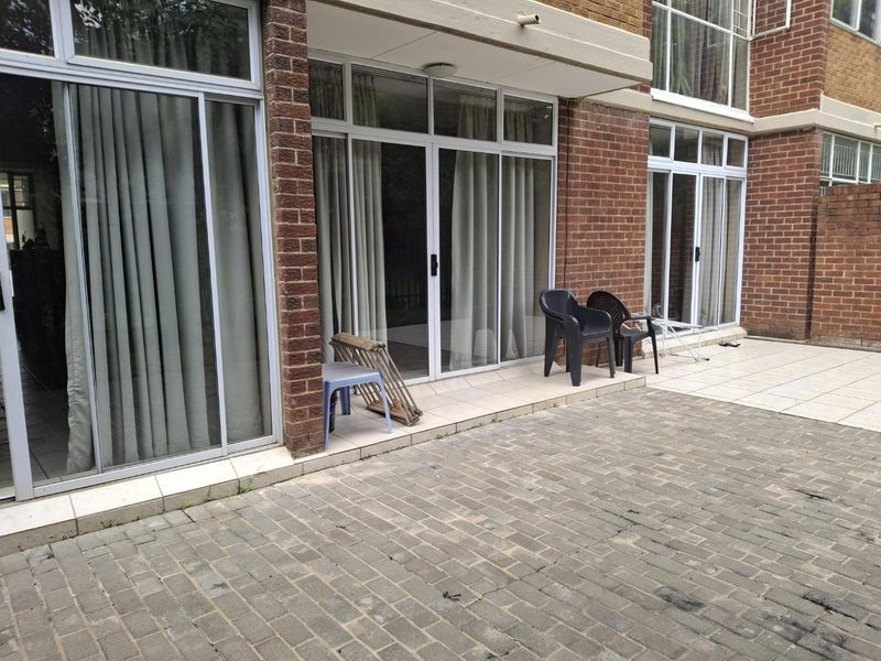A paved outdoor courtyard area featuring a tiled patio section and large sliding glass doors providing access to the apartment interior.