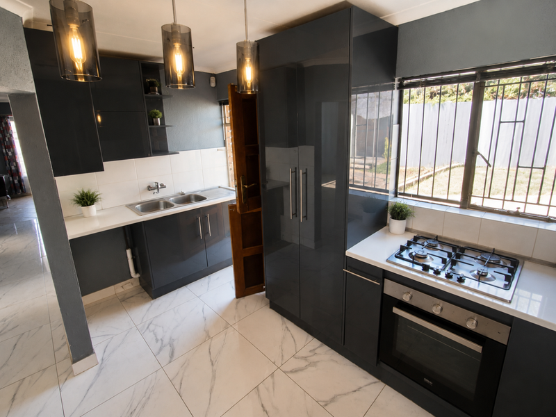 Modern kitchen featuring dark grey cabinetry, marble-look floor tiles, built-in gas hob, oven, and double sink with ample natural light.