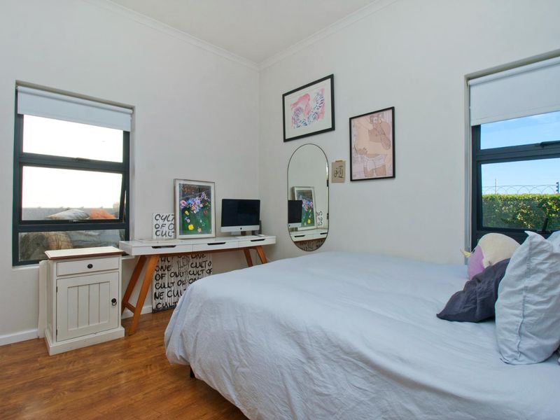 A bright bedroom featuring laminate flooring, dual windows with roller blinds, and neutral wall finishes.