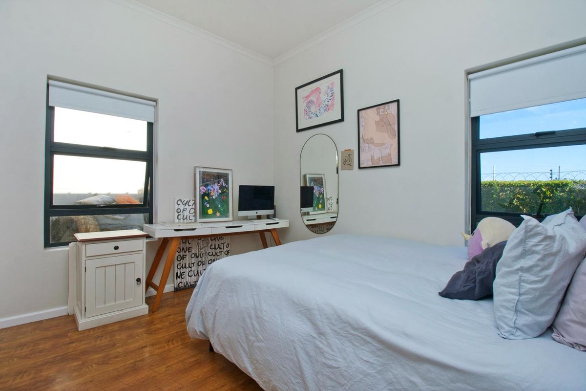 A bright bedroom featuring laminate flooring, dual windows with roller blinds, and neutral wall finishes.