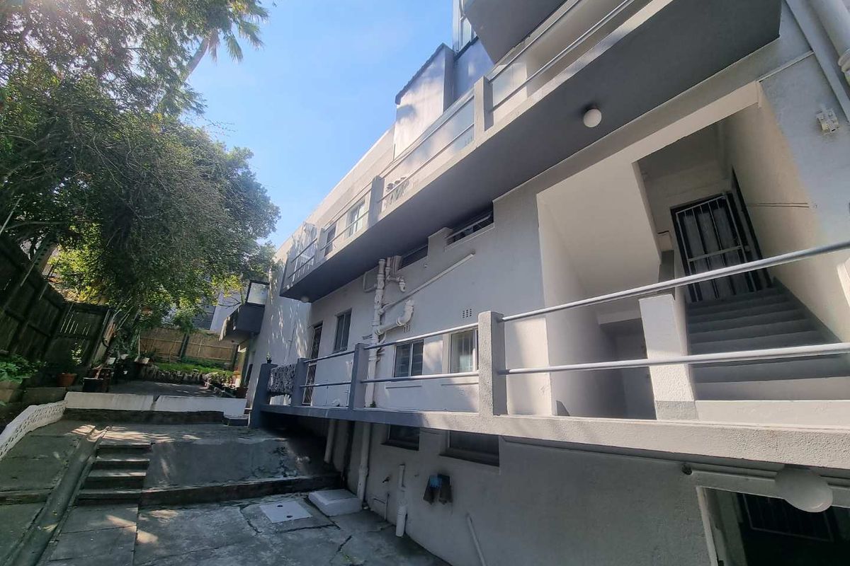 Rear exterior view of the apartment building featuring concrete staircases, metal railings, and paved ground area with visible exterior plumbing.