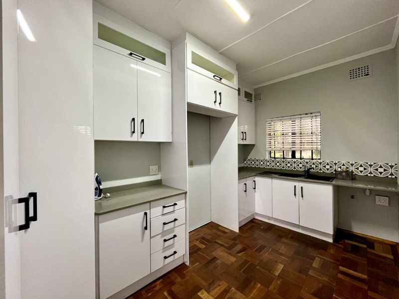 A clean, modern kitchen featuring white cabinetry, stone countertops, a patterned tile backsplash, and classic parquet flooring.