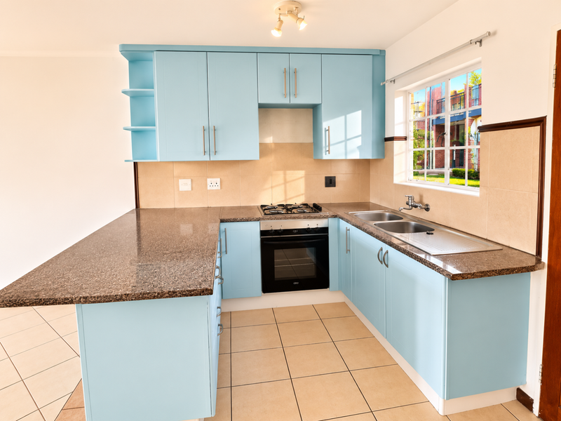 A clean, functional kitchen featuring light blue cabinetry, granite countertops, a gas hob, built-in oven, and tiled flooring.