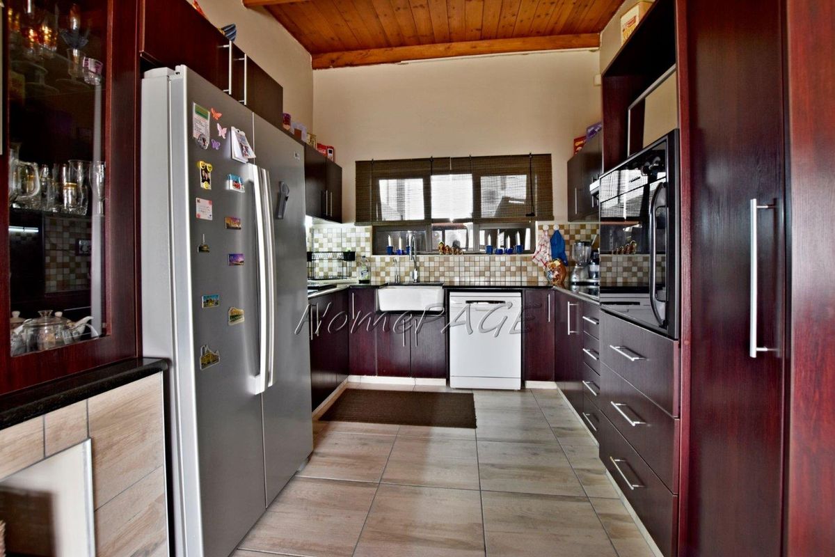 A functional kitchen featuring dark wood cabinetry, tiled backsplash, a farmhouse-style sink, and a timber-paneled ceiling.