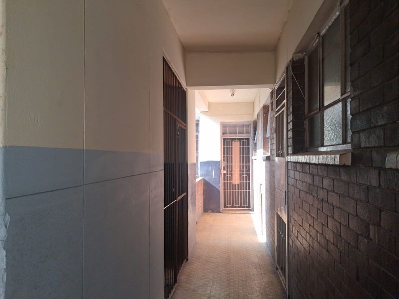A narrow apartment hallway featuring brickwork walls, tiled flooring, and security gates at the entrance points.