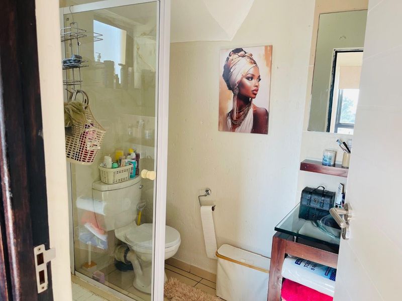 Compact bathroom featuring a glass-enclosed shower, a standard toilet, and a vanity area with a wall-mounted mirror.