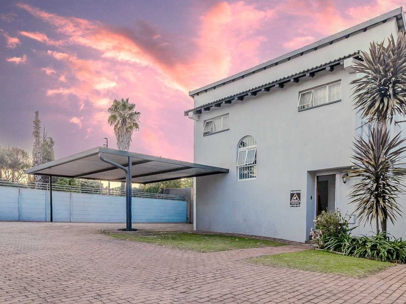 Front exterior view of the townhouse featuring a paved driveway, a covered carport, and a secure perimeter wall.