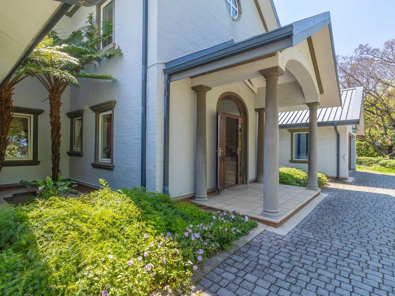 A charming front entrance featuring a covered porch with stone columns, a classic arched doorway, and a well-maintained cobblestone driveway.