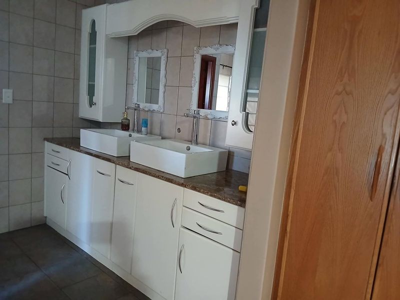 A well-maintained bathroom featuring a double vanity with vessel sinks, granite countertops, and ample built-in cabinetry for storage.