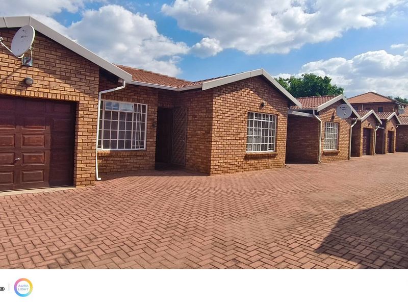 A row of face brick townhouses featuring paved driveways, secure garage access, and tiled roofing in a well-maintained residential complex.
