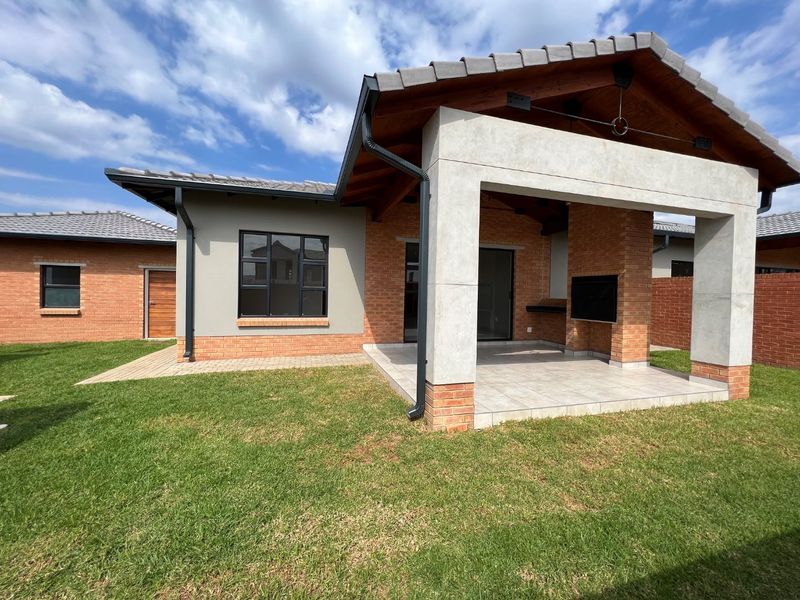 A well-maintained rear exterior featuring a covered patio with a built-in braai, brick and concrete construction, and a neat lawn area.