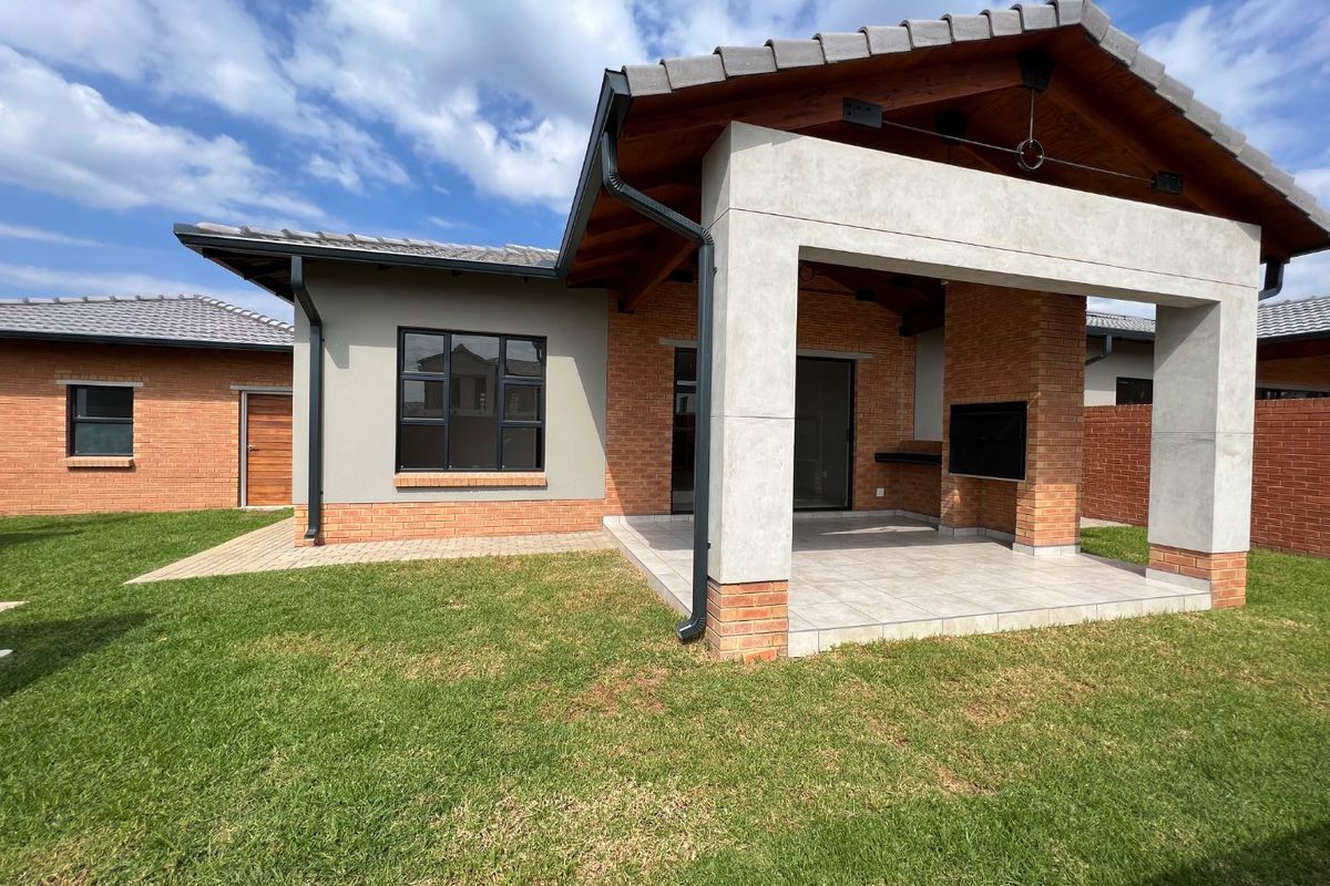 A well-maintained rear exterior featuring a covered patio with a built-in braai, brick and concrete construction, and a neat lawn area.