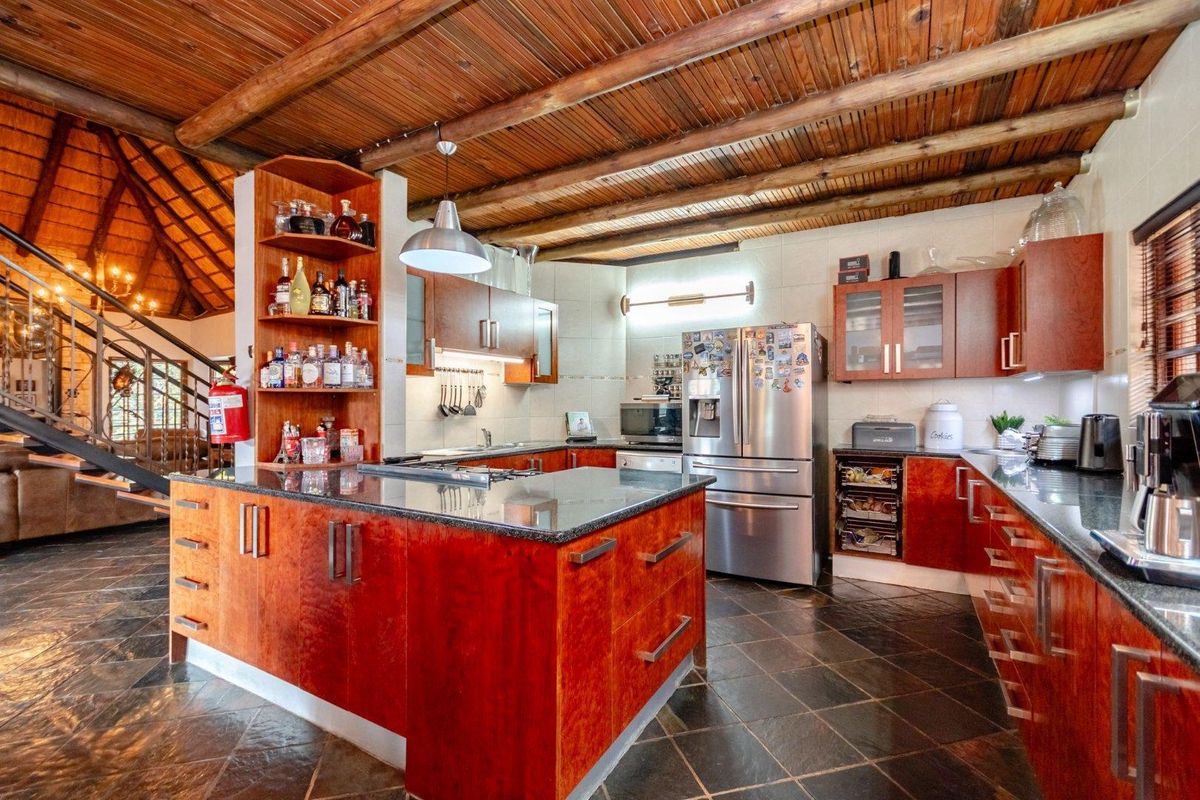 Spacious kitchen featuring rich wooden cabinetry, granite countertops, slate flooring, and a distinctive exposed timber beam ceiling, seamlessly integrated with the open-plan living area.