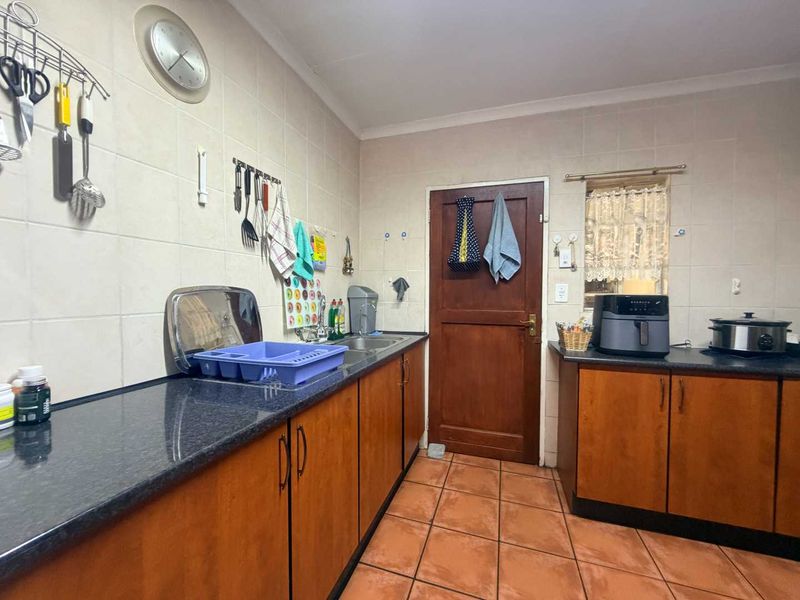 A functional kitchen featuring laminate cabinetry, dark granite countertops, tiled backsplash, and ceramic floor tiles with a classic timber door.