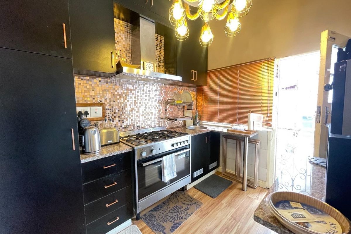 A compact kitchen featuring dark cabinetry, stone countertops, a gas stove with extractor fan, and a decorative mosaic tile backsplash.