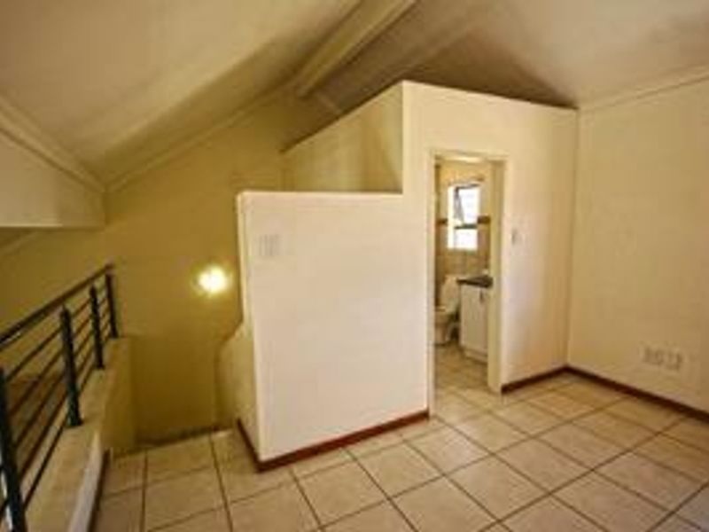 An empty bedroom featuring tiled flooring, a sloped ceiling, a metal balustrade, and an attached en-suite bathroom.