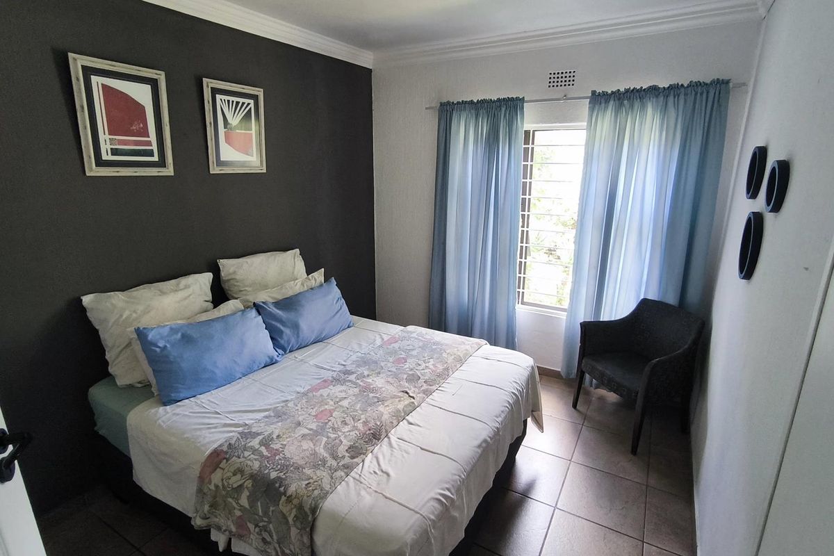 A well-lit bedroom featuring tiled flooring, a dark accent wall, and a window with security bars and curtains.