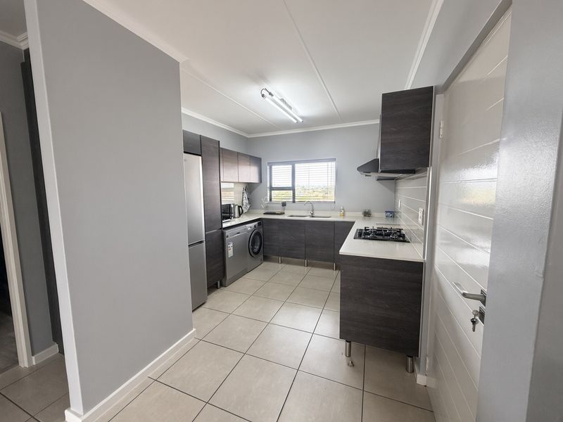 Modern kitchen featuring dark wood cabinetry, light countertops, gas hob, extractor fan, and tiled flooring in a clean, functional layout.