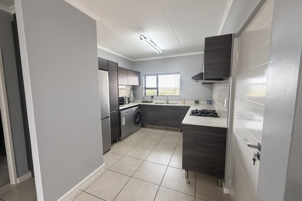Modern kitchen featuring dark wood cabinetry, light countertops, gas hob, extractor fan, and tiled flooring in a clean, functional layout.