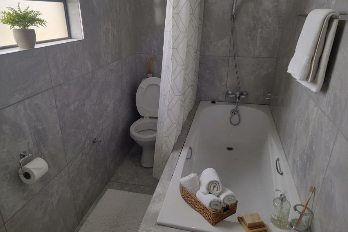 A functional bathroom featuring grey marble-look wall and floor tiles, a built-in bathtub with shower mixer, and a standard toilet.