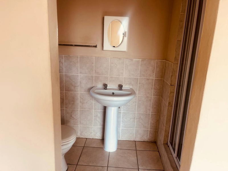 A functional bathroom featuring a pedestal basin, tiled splashback, shower enclosure, and toilet, offering a clean and practical layout.