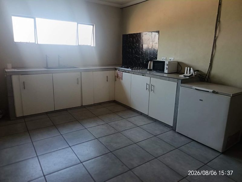 A functional kitchen featuring tiled flooring, built-in cabinetry with tiled countertops, a sink, and a hob with a splashback.