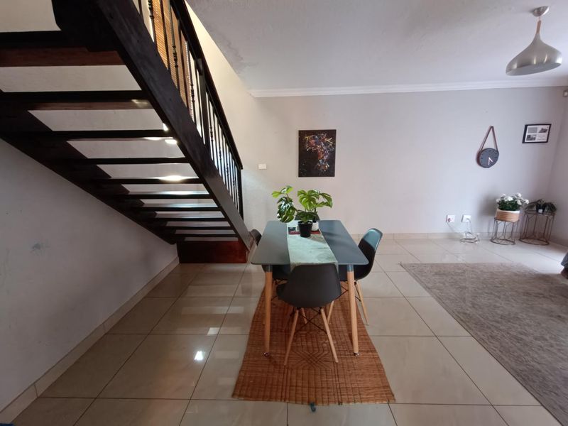 Open plan living and dining area featuring tiled flooring and a prominent wooden staircase with metal balustrades.