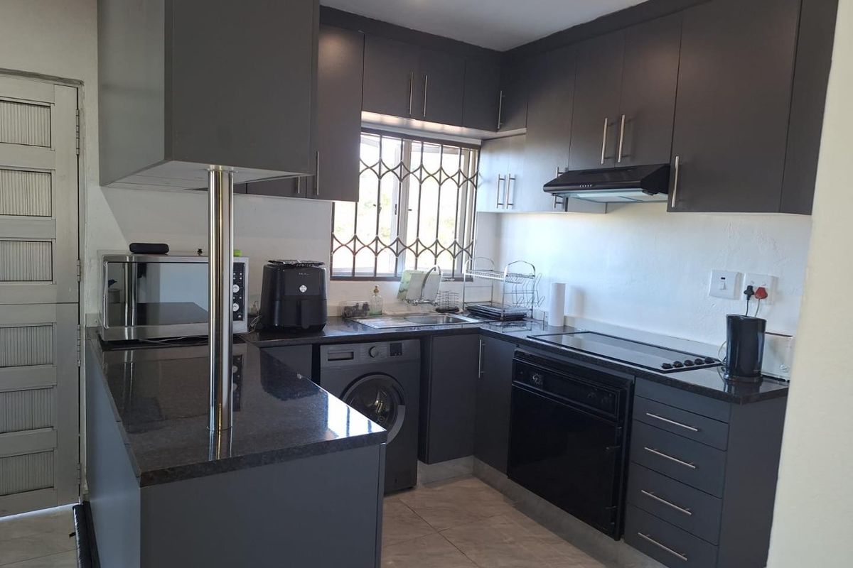 Modern kitchen featuring dark cabinetry, granite countertops, built-in oven, electric hob, extractor fan, and integrated laundry plumbing.