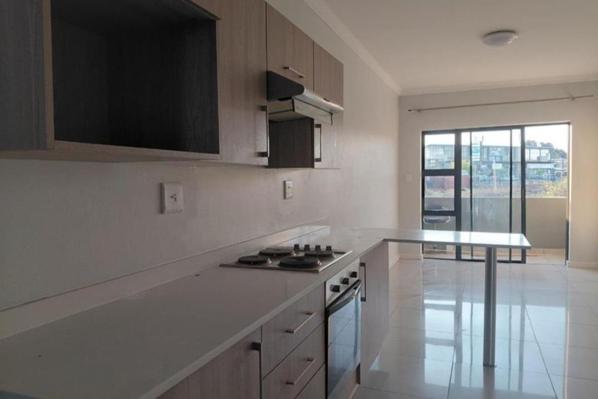 Modern kitchen featuring light wood cabinetry, built-in oven and hob, breakfast bar, and tiled flooring, leading to an outdoor balcony area.