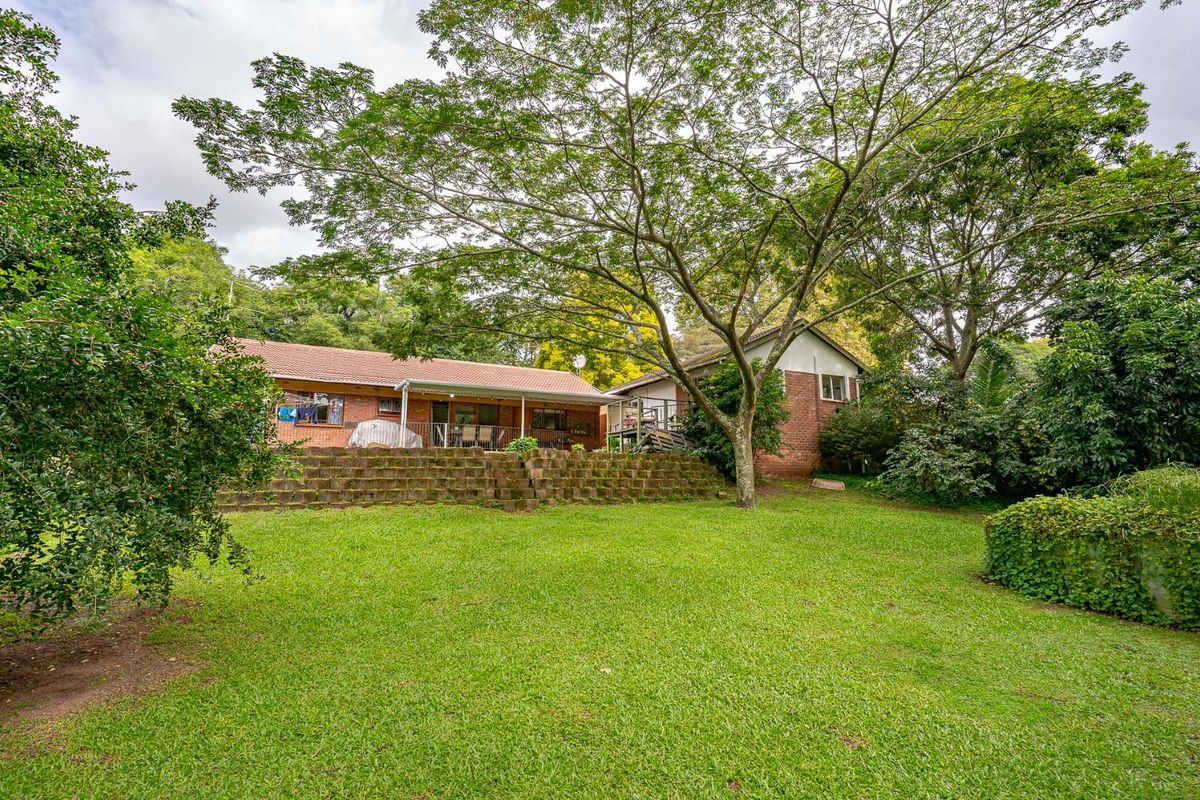 Spacious rear garden featuring a large lawn, mature trees, and a raised brick retaining wall leading to the main house exterior.