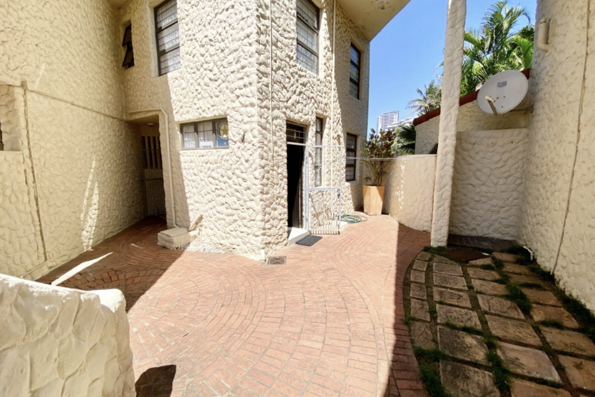 A rear courtyard area featuring stone-clad exterior walls, brick paving, and a stone slab walkway, providing a private outdoor space.