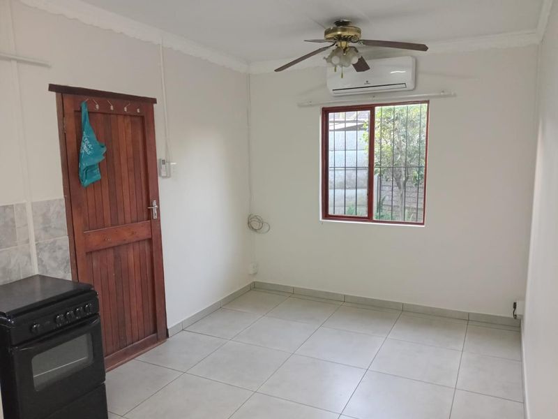 A clean, empty kitchen area featuring tiled flooring, a ceiling fan, split-system air conditioning, and a secure window with burglar bars.