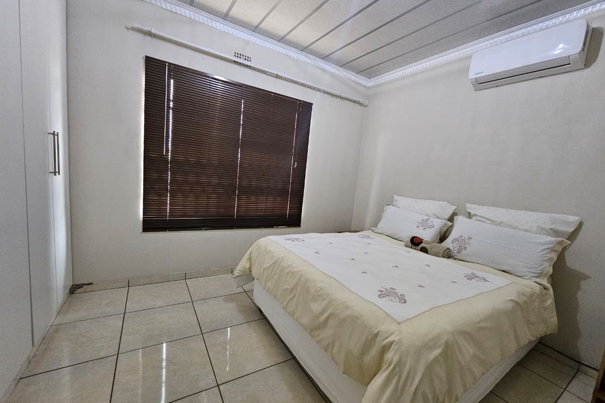 A well-maintained bedroom featuring tiled flooring, built-in wardrobes, a split-system air conditioner, and venetian blinds for privacy.