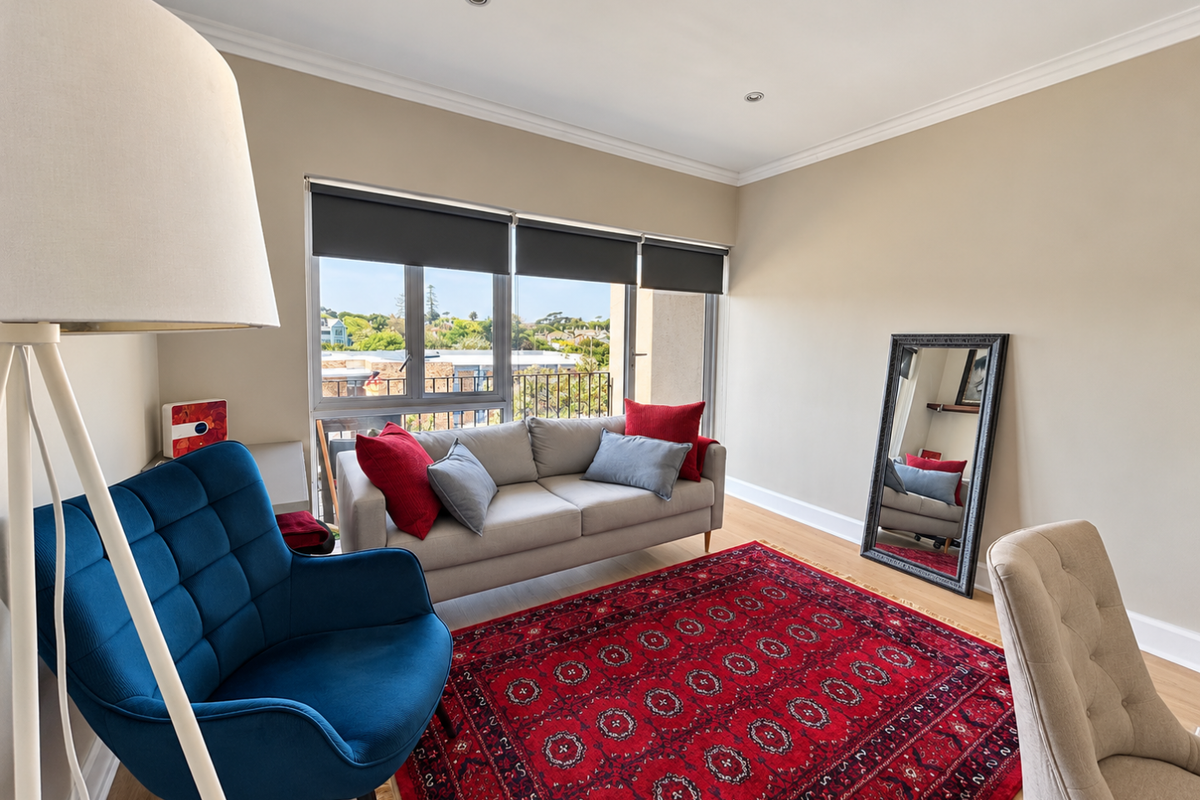 A bright and well-maintained living room featuring neutral walls, recessed lighting, and large windows with roller blinds, offering a pleasant outlook.