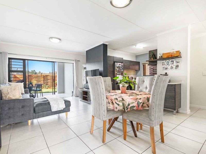 Bright open-plan living and dining area featuring tiled floors, modern kitchen cabinetry, and large sliding doors leading to an outdoor patio space.