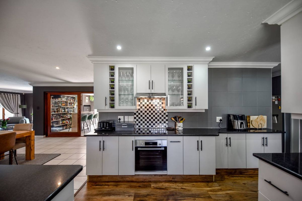 Modern kitchen featuring white cabinetry, granite countertops, a checkered tile splashback, built-in oven, and integrated extractor fan with recessed lighting.