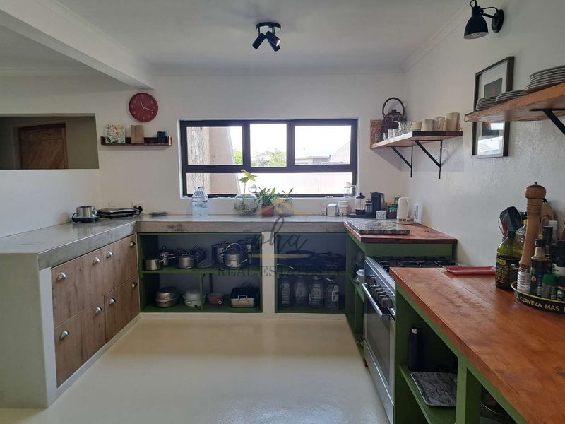 A functional kitchen featuring a mix of concrete and wooden countertops, open shelving, and a gas stove with built-in cabinetry.