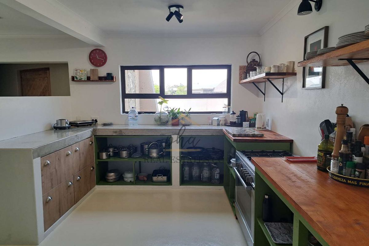 A functional kitchen featuring a mix of concrete and wooden countertops, open shelving, and a gas stove with built-in cabinetry.
