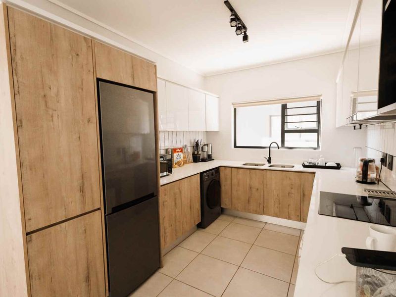 Modern kitchen featuring wood-grain and white cabinetry, subway tile backsplash, double sink, electric hob, and tiled flooring with integrated appliance space.
