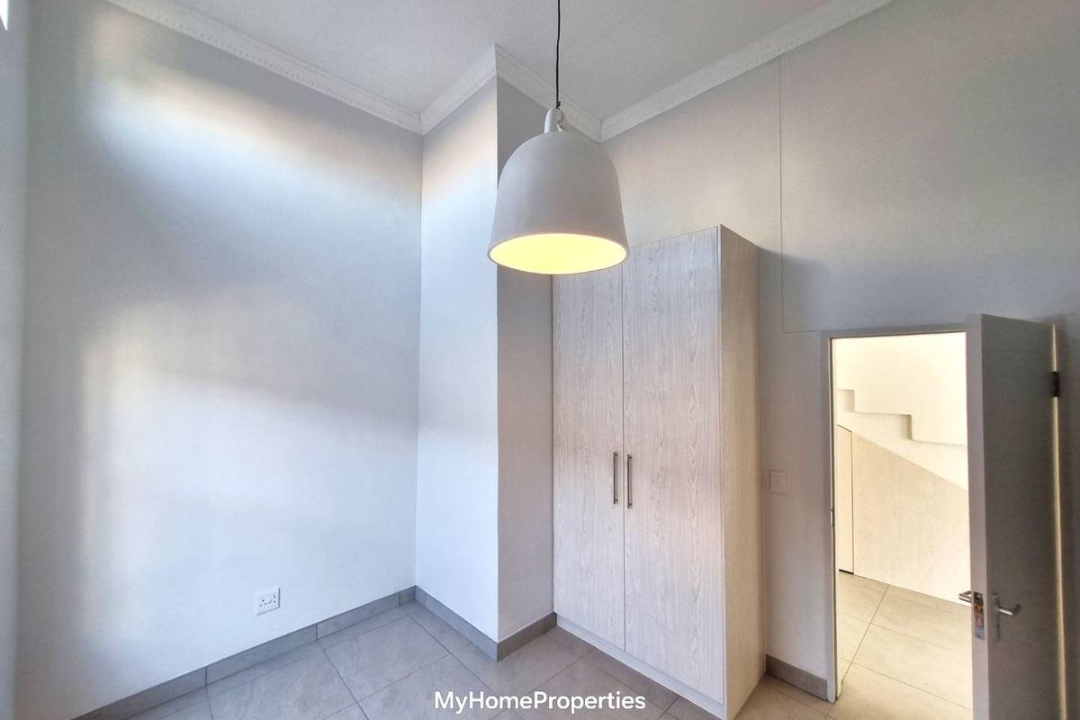 A bright, empty bedroom featuring neutral tiled flooring, a modern built-in wardrobe, and a contemporary pendant light fixture.
