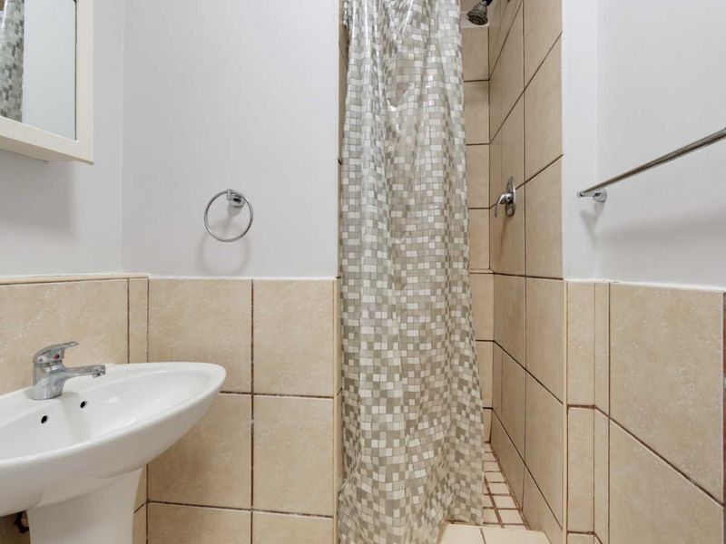 A functional bathroom featuring a pedestal sink, a tiled shower enclosure with a mixer, and wall-mounted fixtures.