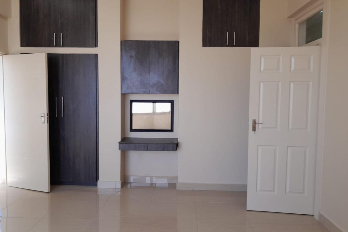 A clean, empty bedroom featuring dark wood built-in cupboards, a matching floating vanity with mirror, and neutral tiled flooring.
