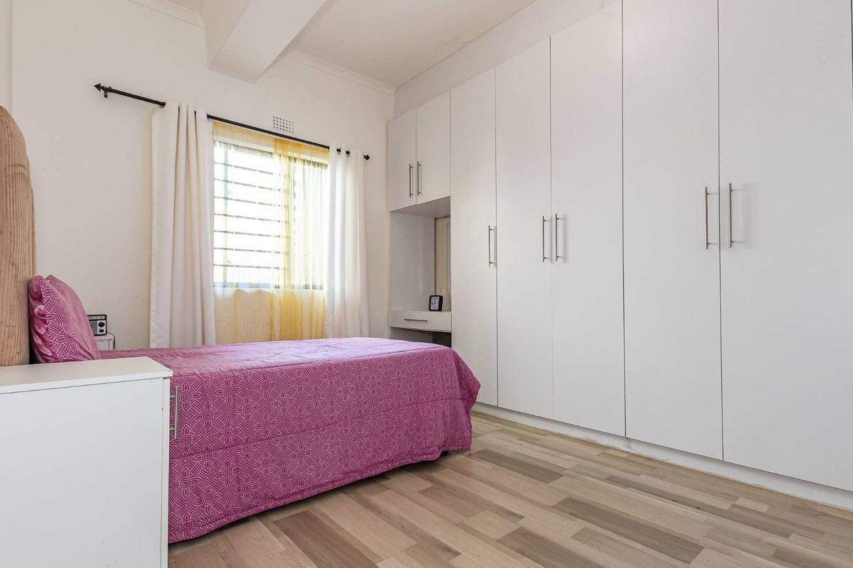 A well-maintained bedroom featuring extensive floor-to-ceiling built-in cupboards, modern laminate flooring, and a window fitted with security burglar bars.