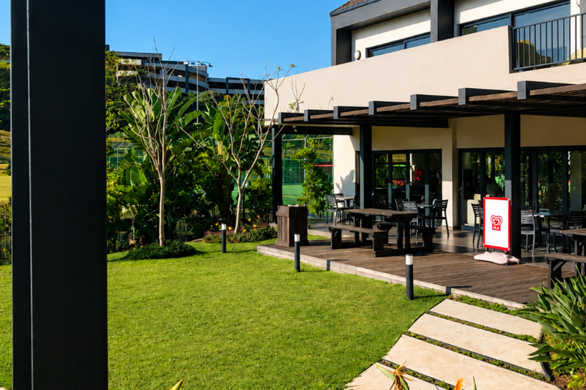 A well-maintained rear exterior area featuring a timber deck with a pergola, landscaped garden, and a paved walkway leading to the building.