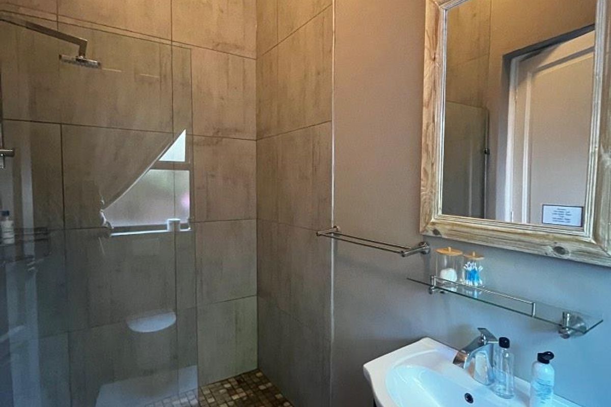 A modern bathroom featuring a walk-in shower with glass screen, mosaic floor tiling, and a vanity basin with a wall-mounted mirror.
