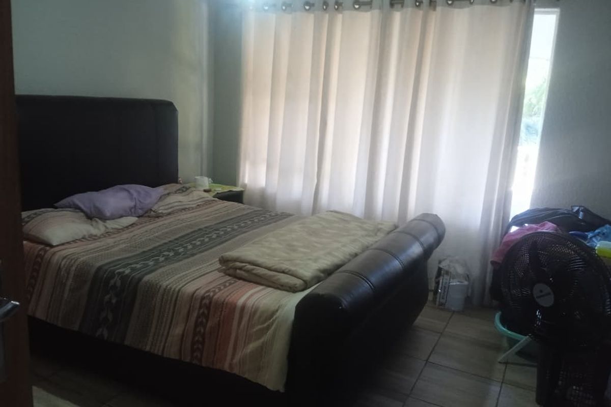 A bedroom featuring tiled flooring and a large window with curtains, providing natural light to the space.