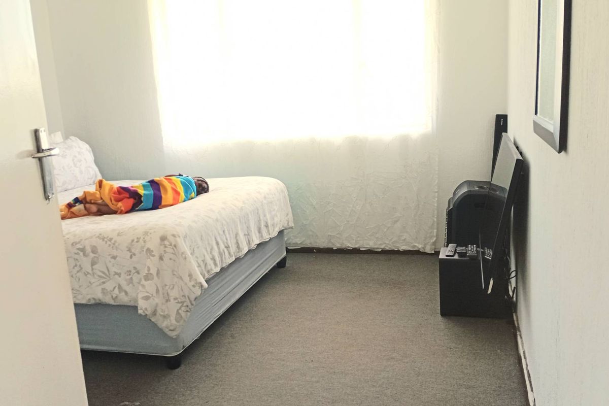 A simple bedroom featuring carpeted flooring and a large window allowing for natural light.